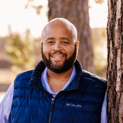 Close-up outdoor headshot portrait of Dr. Talon Davis smiling in a blue vest.