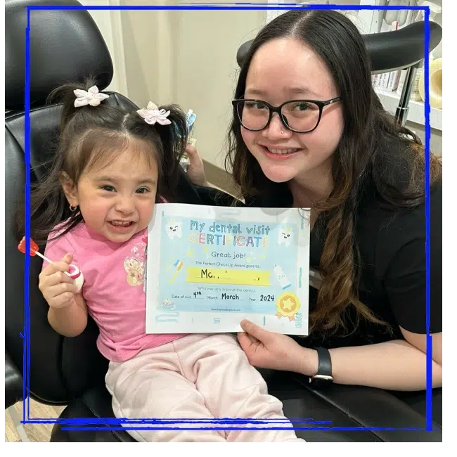Young patient holding a dental visit certificate with a team member at Spanaway Children's Dentistry near Eatonville