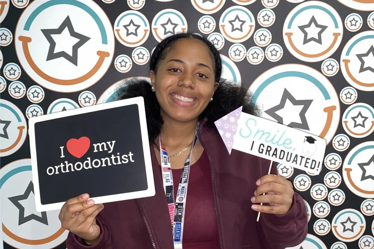 Teen girl holding an orthodontic treatment graduation sign