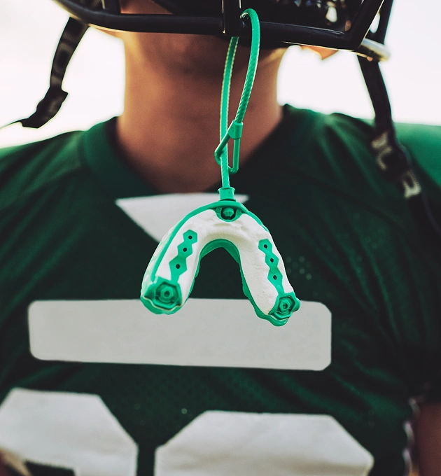 Athlete in a helmet and green jersey holding a custom sports mouthguard for tooth protection