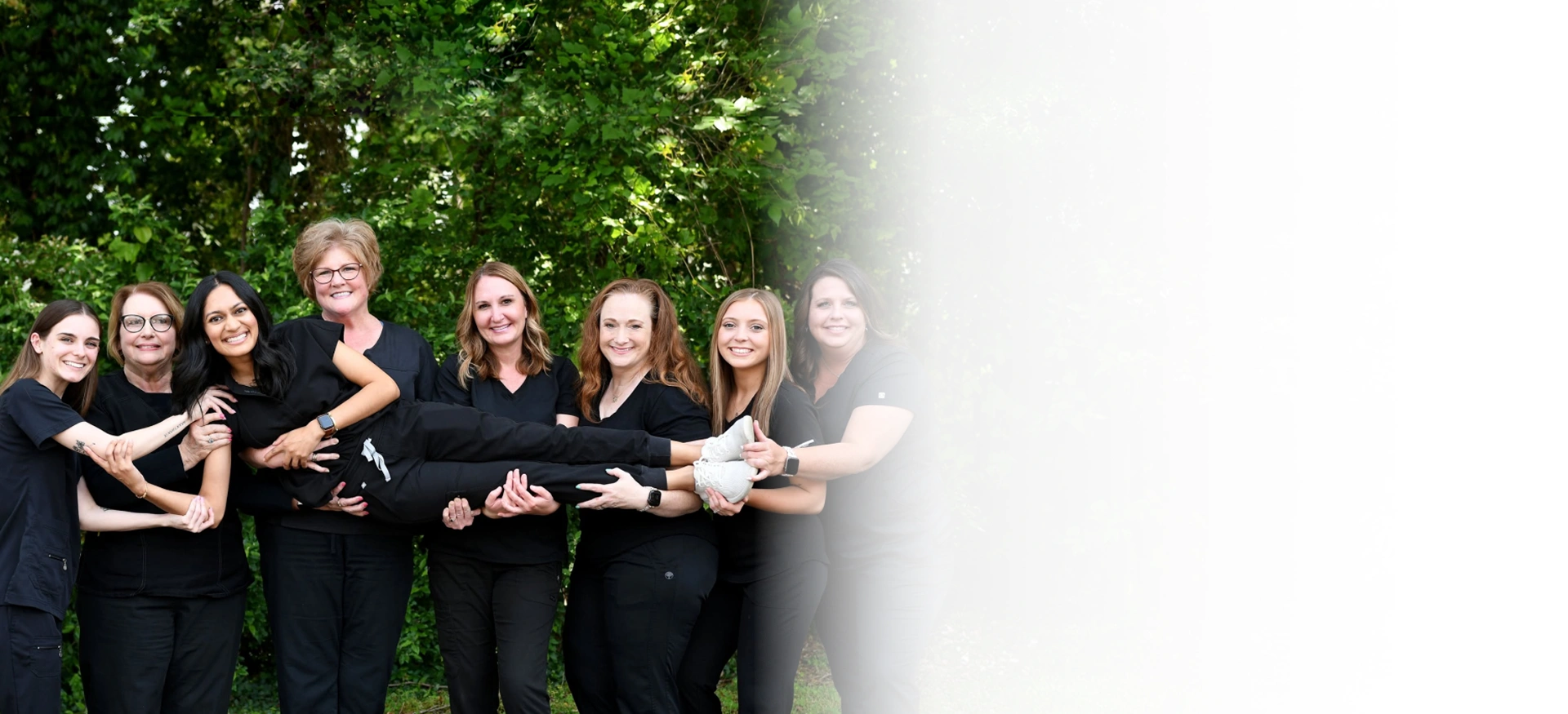 White Rose Dentistry team of eight dental professionals in black attire standing together outdoors in York, SC.
