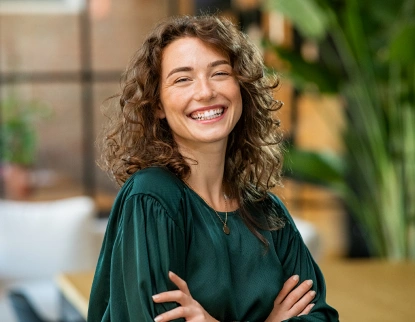 Smiling woman with curly hair wearing a teal shirt in a dental office setting.
