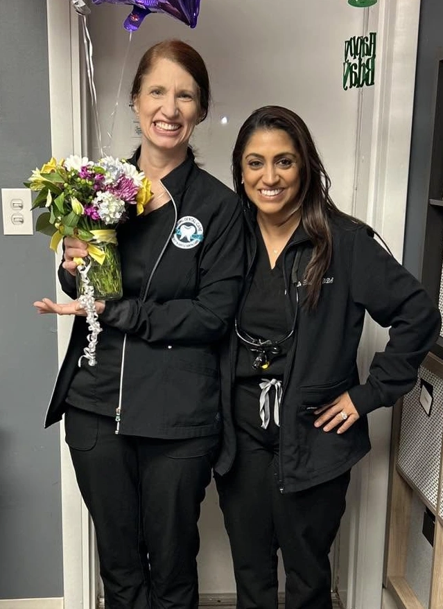 Two dental professionals in black jackets celebrate with a colorful flower bouquet in Aurora.