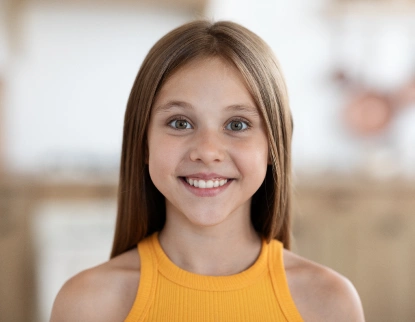 Smiling young girl in yellow top, pediatric dental patient portrait for Aurora dental practice.